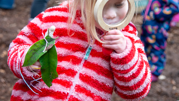 child looks through magnifying glass in woods